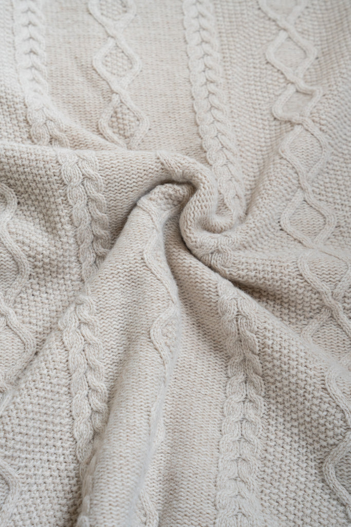 Beige plaid van 100% merinowol, 130 x 170 cm, vlechtmotief, gefotografeerd als close-up van textuur en kleur.