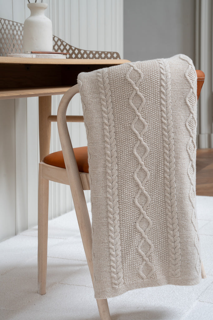 Vlechtmotief beige plaid van 100% merinowol, 130 x 170 cm, elegant over een stoel gehangen in een Scandinavisch interieur met een bureau op de achtergrond.