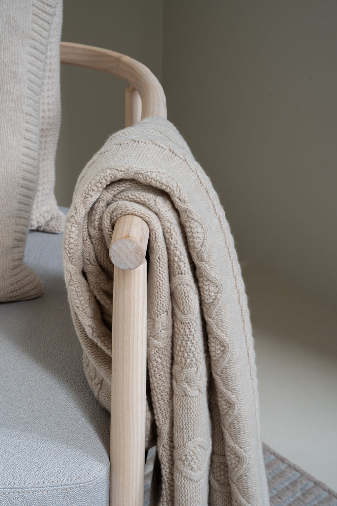 Vlechtmotief beige plaid van 100% merinowol, 130 x 170 cm, nonchalant over de leuning van een houten loungestoel een close-up. 