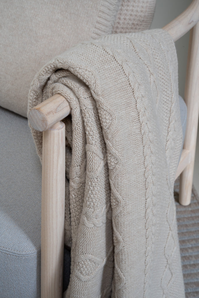 Vlechtmotief beige plaid van 100% merinowol, 130 x 170 cm, nonchalant over de leuning van een houten loungestoel een close-up. 