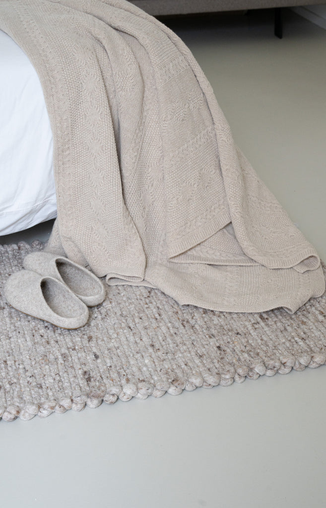 Vlechtmotief beige plaid van 100% merinowol, 130 x 170 cm, nonchalant over bed gelegd. 