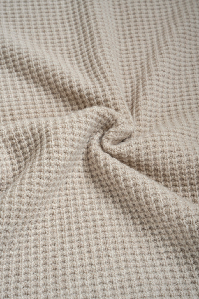 Beige plaid van 100% merinowol, 130 x 170 cm, met wafelpatroon, gefotografeerd als close-up van textuur en kleur.