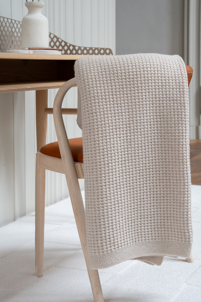 Beige plaid van 100% merinowol met wafelpatroon, 130 x 170 cm, elegant over een stoel gehangen in Scandinavisch interieur met bureau op de achtergrond.