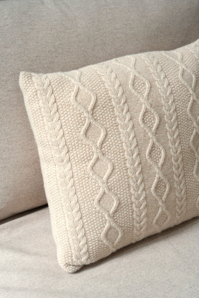 Sfeerbeeld van een beige sierkussen 50 x 50 cm met Aran-kabelpatroon van 100% merinowol, subtiel gestyled op een stijlvolle neutrale zetel.