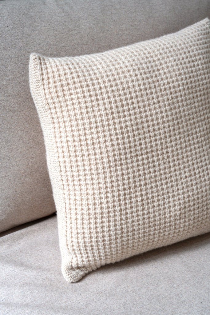 Sfeerbeeld van een beige sierkussen in 100% merinowol met wafelpatroon, rustend op een neutrale zetel.