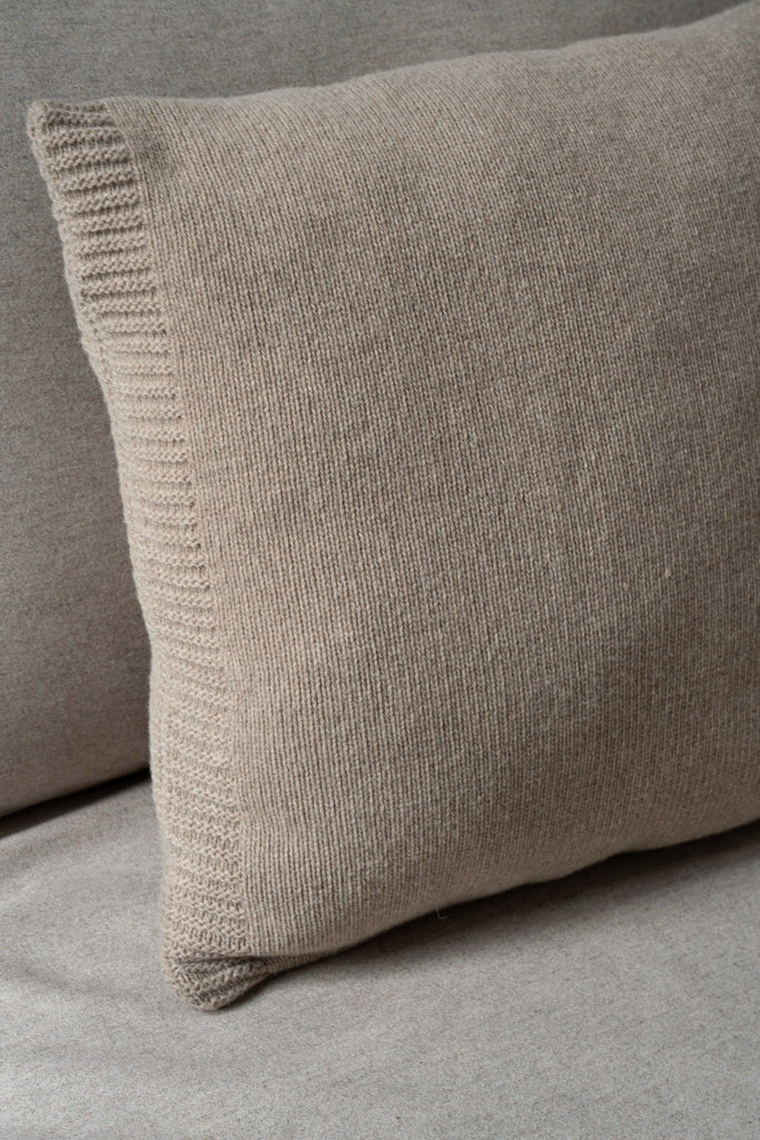 Bruin sierkussen van 100% gladgebreide merinowol, 50 x 550 cm, liggend op een neutrale zetel.