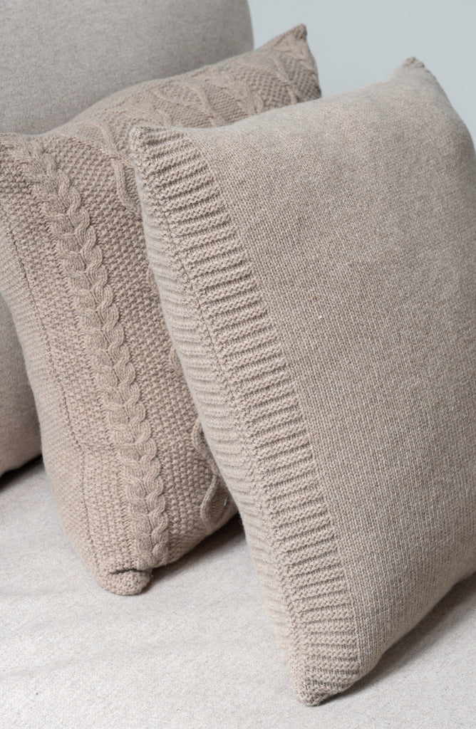 Twee bruine sierkussens gemaakt uit 100% merinowol, 50 x 50  cm, leunend tegen een neutrale beige/bruine zetel.