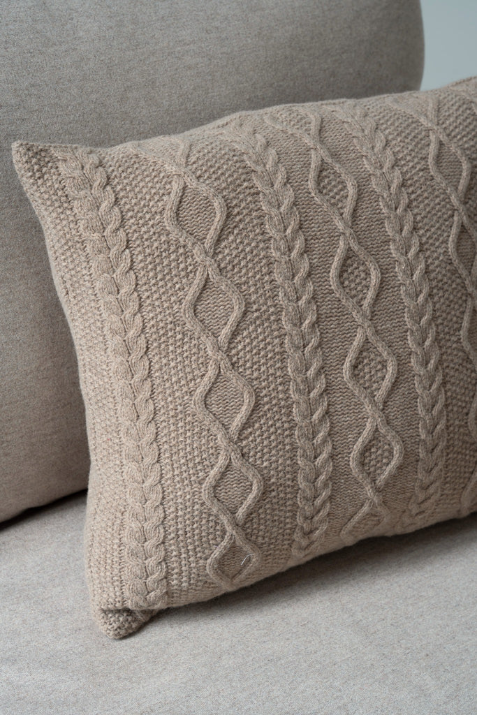 Sfeerbeeld van kabelpatroon bruin sierkussen van 100% merinowol, 50 x 50 cm, gestyled op een neutrale zetel.
