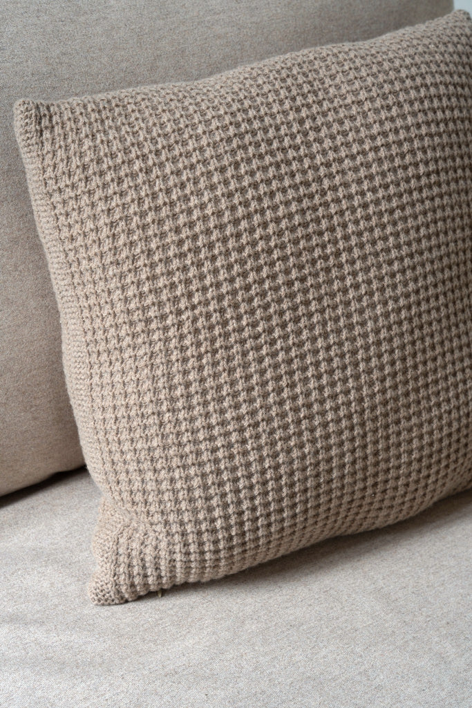 Bruin sierkussen van 100% merinowol met wafelpatroon, subtiel gestyled in een stijlvolle neutrale zetel.