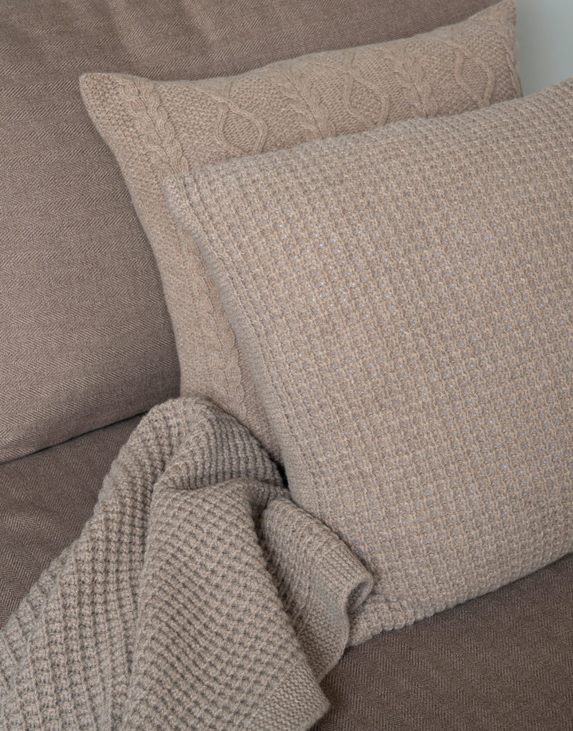 Sfeerbeeld van bruine sierkussens van 100% merinowol met wafel- en glad breisel, geplaatst in een moderne zetel van natuurlijke materialen.