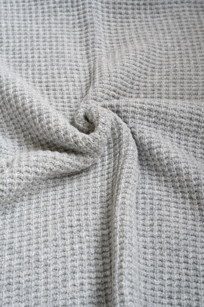 Grijze plaid van 100% merinowol, 130 x 170 cm, met wafelpatroon, gefotografeerd als close-up van textuur en kleur.