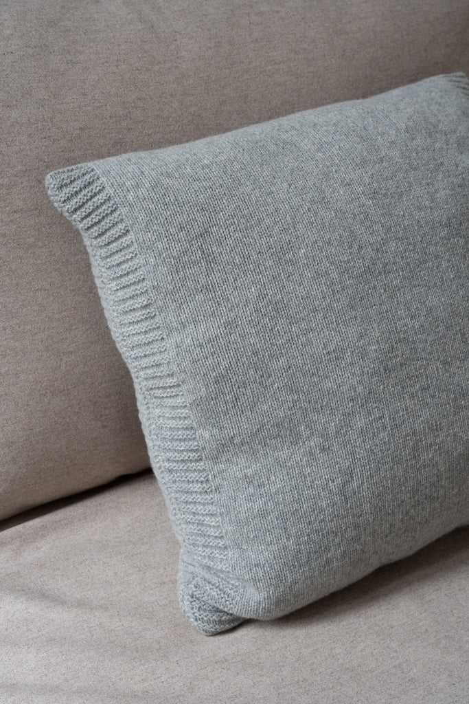 Grijs merinowollen sierkussen liggend op een klassieke zetel, 50 x 50 cm, sfeervol gestyled in een lichte, neutrale omgeving.