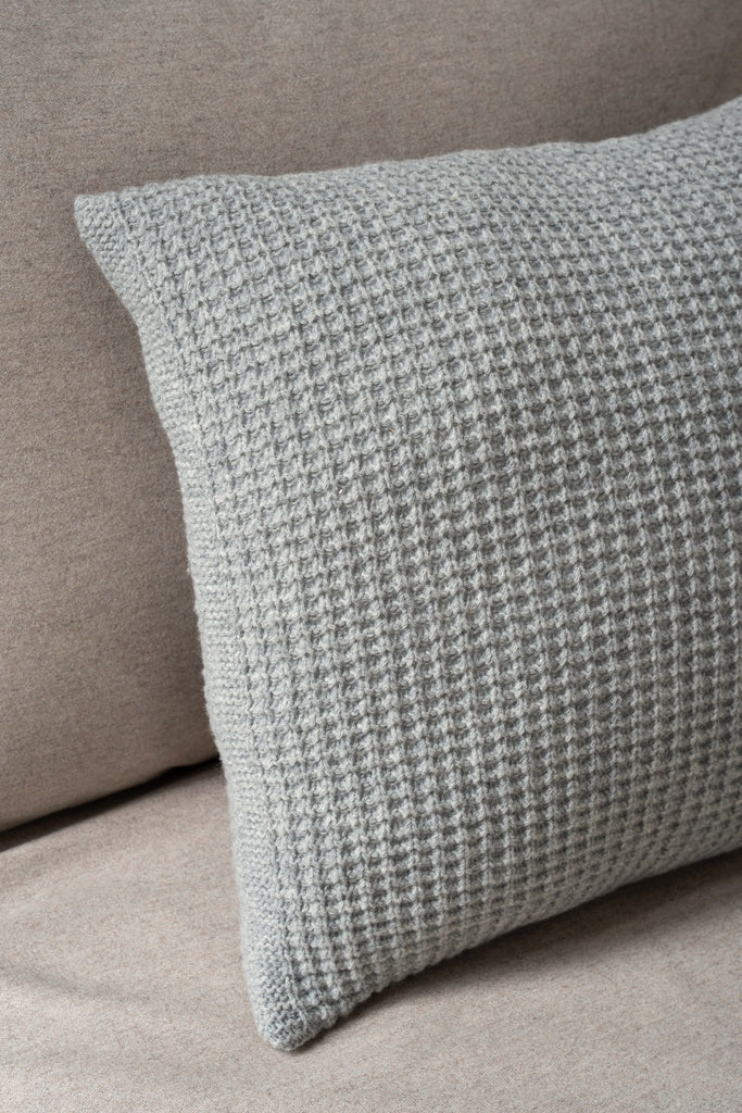 Grijs sierkussen van 100% merinowol met wafelpatroon, subtiel gestyled in een neutrale zetel.
