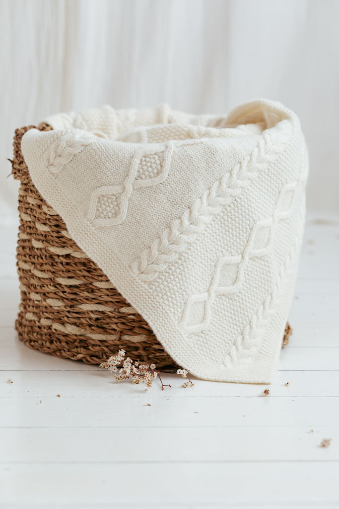 Vlechtmotief witte plaid van 100% merinowol, 130 x 170 cm, losjes in een houten mand geplaatst.