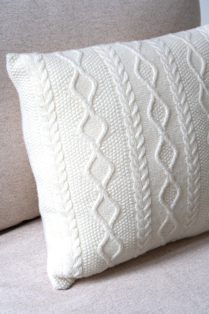 Klassiek Aran-kabelpatroon wit sierkussen van 100% merinowol, 50 x 50 cm, subtiel gestyled in een neutrale zetel.