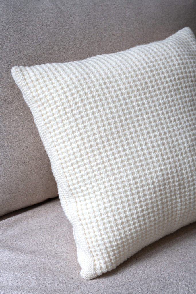 Wit sierkussen van 100% merinowol met wafelpatroon, subtiel gestyled in een stijlvolle neutrale zetel.
